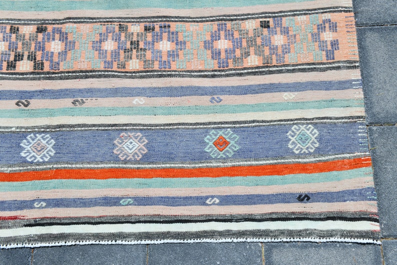 May include: A handwoven rug with a striped pattern in shades of blue, orange, pink, and green. The rug has a fringe border.