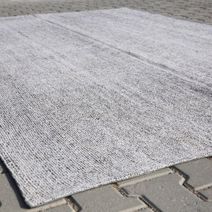 May include: A gray and white woven rug with a textured surface. The rug is laid out on a gray concrete surface.