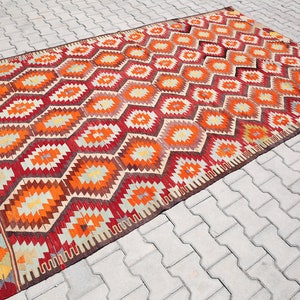 May include: A traditional Turkish rug with a geometric pattern in shades of red, orange, yellow, and brown. The rug has a woven border and is made of wool.