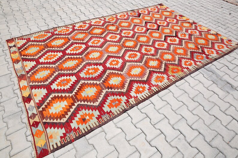May include: A traditional Turkish rug with a geometric pattern in shades of red, orange, yellow, and brown. The rug has a woven border and is made of wool.