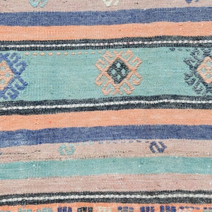 May include: A woven rug with a striped pattern in shades of blue, pink, and green. The rug features a repeating geometric design in the center of each stripe.