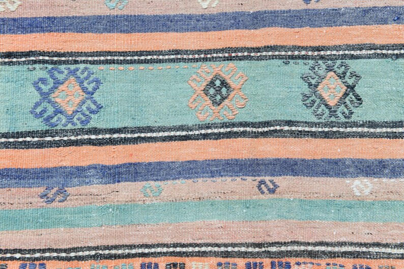 May include: A woven rug with a striped pattern in shades of blue, pink, and green. The rug features a repeating geometric design in the center of each stripe.