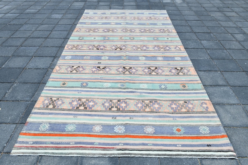 May include: A vintage rug with a striped pattern in shades of blue, green, pink, and orange. The rug has a geometric design with small diamond shapes and floral motifs.