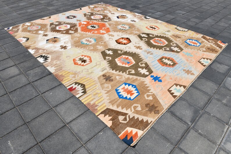 May include: A vintage Turkish rug with a geometric pattern in shades of brown, orange, blue, and white. The rug has a distressed look and is laid out on a gray tiled floor.