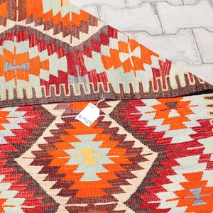 May include: A colorful, geometric patterned rug with a brown border. The rug is folded in half and has a price tag attached to it that reads "K-4525".