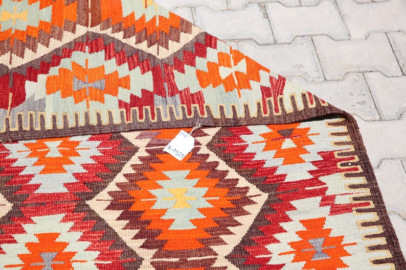 May include: A colorful, geometric patterned rug with a brown border. The rug is folded in half and has a price tag attached to it that reads "K-4525".