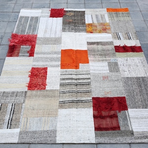 Può includere: Un tappeto patchwork con una varietà di colori e trame. Il tappeto è composto da diversi pezzi di tessuto cuciti insieme, creando un design unico e interessante. Il tappeto è principalmente bianco e grigio, con accenti di rosso, arancione e marrone.