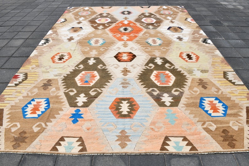 May include: A vintage Turkish rug with a geometric pattern in shades of brown, orange, blue, and white. The rug has a distressed look with faded colors and a worn texture.