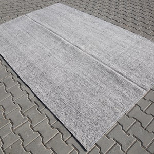 May include: A gray area rug with a subtle textured pattern. The rug is folded in half and laid out on a gray brick surface.