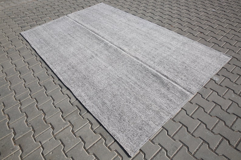 May include: A gray area rug with a subtle textured pattern. The rug is folded in half and laid out on a gray brick surface.