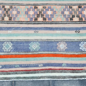 May include: A handwoven rug with a striped pattern in shades of blue, orange, green, and white. The rug has a geometric design with small squares and diamonds.