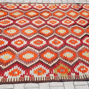 May include: A traditional Turkish rug with a geometric pattern in shades of red, orange, beige, and brown. The rug has a fringe border.