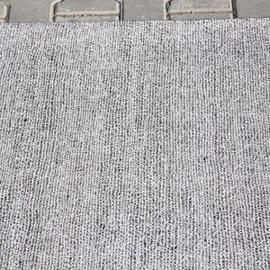 May include: A close-up of a gray and white woven rug with a textured surface.