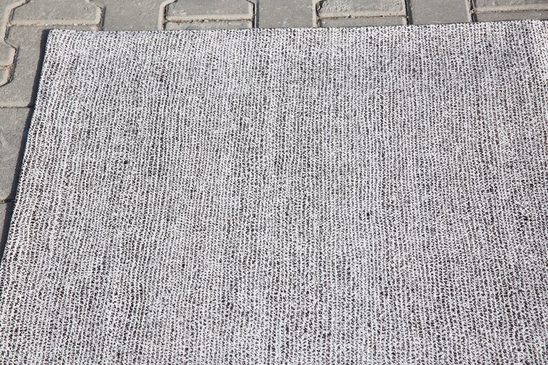 May include: A close-up of a gray and white woven rug with a textured surface.