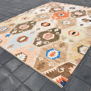 May include: A beige, brown, blue, and orange patterned rug with a geometric design. The rug is made of wool and has a hand-woven texture.