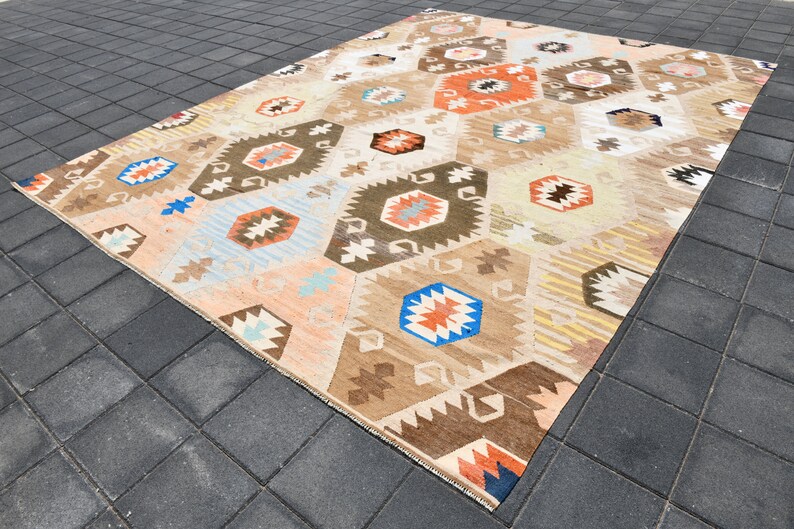 May include: A beige, brown, blue, and orange patterned rug with a geometric design. The rug is made of wool and has a hand-woven texture.