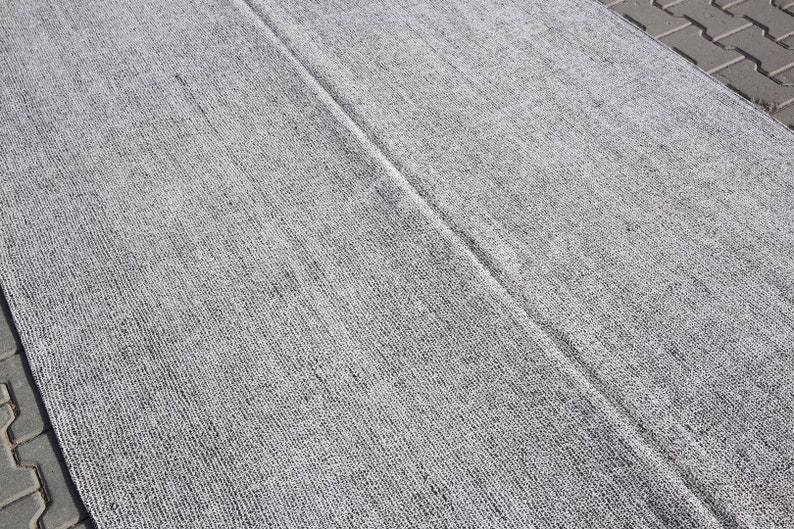 May include: A close-up of a gray and white textured rug with a subtle sheen. The rug has a woven appearance and is made of a soft, comfortable material.