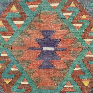 Pu&ograve; includere: Primo piano di un tappeto tessuto colorato con un motivo geometrico di triangoli e rombi in tonalit&agrave; di rosso, blu, verde e giallo.