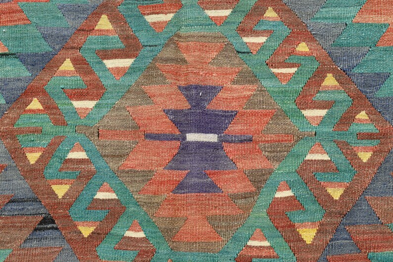 Pu&ograve; includere: Primo piano di un tappeto tessuto colorato con un motivo geometrico di triangoli e rombi in tonalit&agrave; di rosso, blu, verde e giallo.