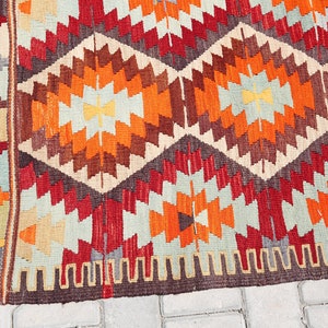 May include: A colorful rug with a geometric pattern in shades of red, orange, brown, and beige. The rug has a fringe border.