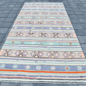 May include: A long, rectangular rug with a striped pattern in shades of blue, green, pink, and orange. The rug has a traditional, handwoven look and is made of natural fibers.