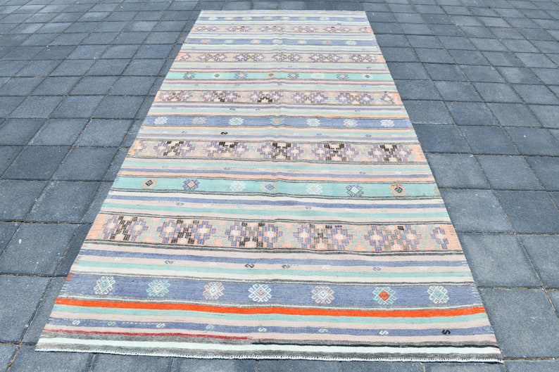 May include: A long, rectangular rug with a striped pattern in shades of blue, green, pink, and orange. The rug has a traditional, handwoven look and is made of natural fibers.