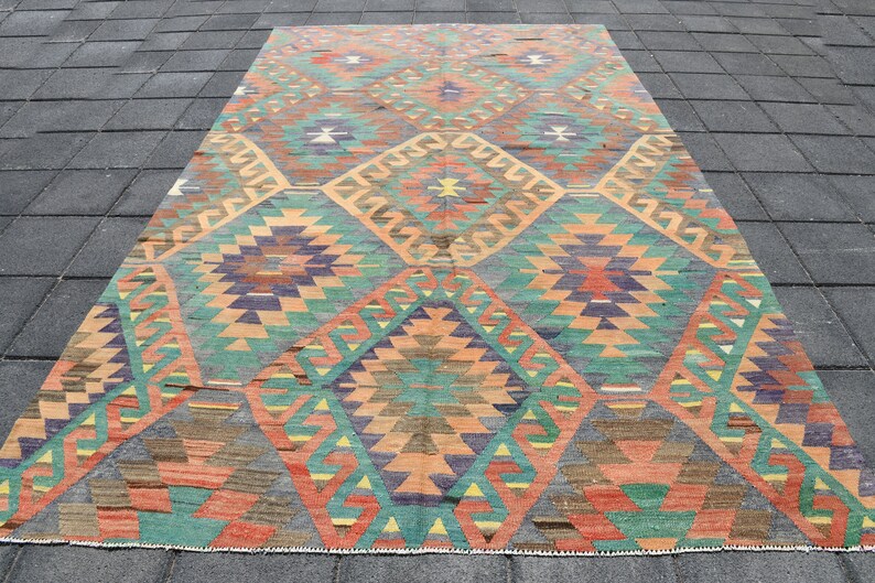 Pu&ograve; includere: Un tappeto vintage con un motivo geometrico in tonalit&agrave; arancio, verde, blu e marrone. Il tappeto ha un design a forma di diamante con dettagli intricati.