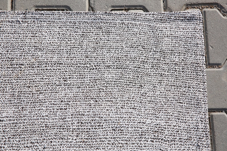 May include: A close-up of a white and gray woven rug with a textured surface.