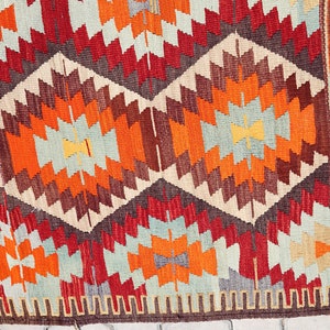 May include: A colorful rug with a geometric pattern in shades of red, orange, brown, and blue. The rug has a fringe border.