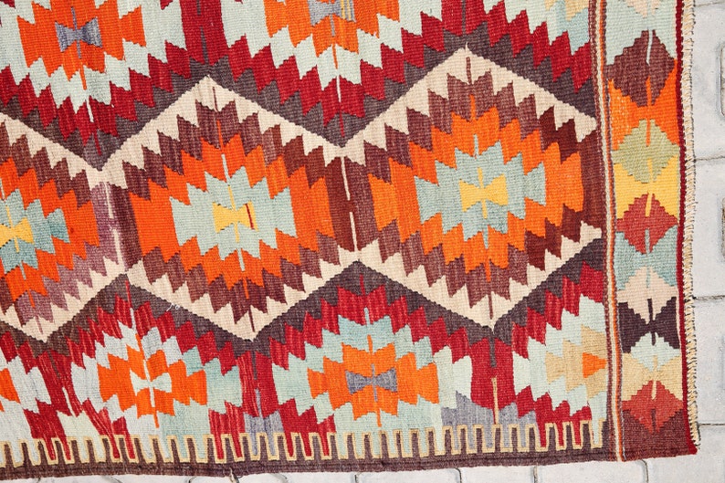 May include: A colorful rug with a geometric pattern in shades of red, orange, brown, and blue. The rug has a fringe border.