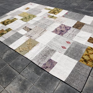 May include: A patchwork rug with a variety of colors and patterns, including white, gray, brown, green, and purple. The rug is made of different fabrics and textures, creating a unique and eclectic look.