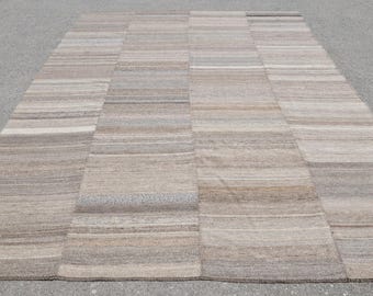 Op de afbeelding: Een rechthoekig patchwork vloerkleed in neutrale tinten. Het kleed bestaat uit verschillende rechthoekige panelen, elk met horizontale strepen in tinten beige, grijs en bruin. Het ontwerp is eenvoudig en modern, met afmetingen in cm.