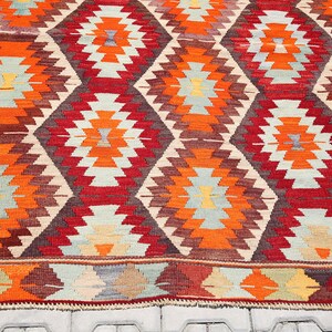 May include: A traditional Turkish rug with a geometric pattern in shades of red, orange, brown, and beige. The rug has a diamond-shaped design with intricate details.