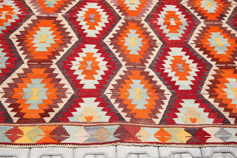 May include: A traditional Turkish rug with a geometric pattern in shades of red, orange, brown, and beige. The rug has a diamond-shaped design with intricate details.