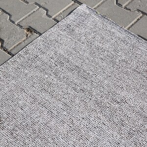 May include: A close-up of a gray and white woven rug with a textured surface.