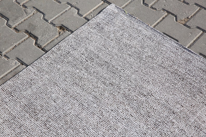 May include: A close-up of a gray and white woven rug with a textured surface.