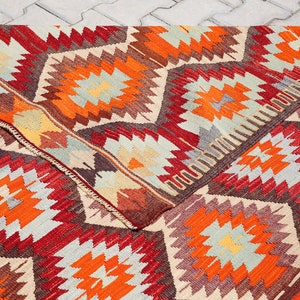 May include: A colorful rug with a geometric pattern in shades of red, orange, brown, and beige. The rug has a traditional design with a repeating pattern of stars and diamonds.