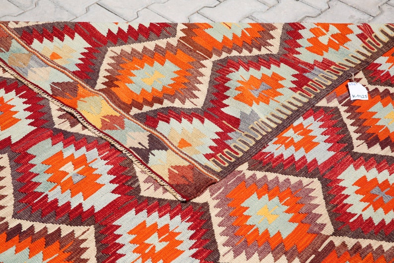 May include: A colorful rug with a geometric pattern in shades of red, orange, brown, and beige. The rug has a traditional design with a repeating pattern of stars and diamonds.