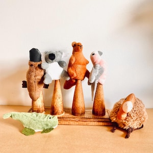 May include: Five plush finger puppets of Australian animals on wooden stands. The animals are a koala, a platypus, a kangaroo, a cockatoo, and a kiwi.