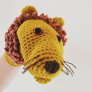 May include: A crocheted lion puppet with a brown nose, black eyes, and a brown mane. The puppet is yellow and has a hand inside to operate it.