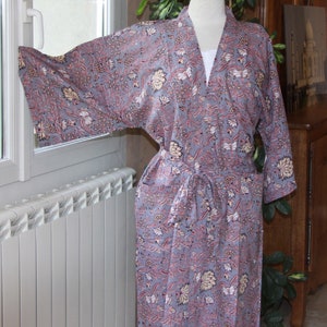 May include: A gray floral print robe with a matching belt. The robe features a V-neck and long sleeves. The floral pattern includes pink, cream, and white accents. The robe is displayed on a mannequin.