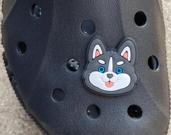 May include: Black clog with a blue-eyed husky dog charm. The charm is made of plastic and has a white face with a pink tongue.