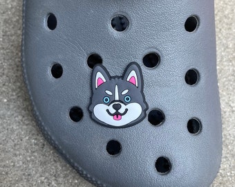 May include: A gray and black cartoon husky dog charm with pink tongue and blue eyes. The charm is attached to a gray shoe.