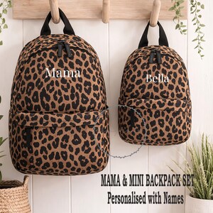 May include: Two leopard print backpacks, one larger and one smaller, suspended from a wooden rack. The larger backpack is labelled "Mama", the smaller one "Bella". The set is labelled "MAMA & MINI BACKPACK SET Personalised with Names."