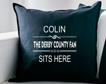 May include: Black throw pillow with white text that reads "COLIN THE DERBY COUNTY FAN SITS HERE" with a stylized football graphic.