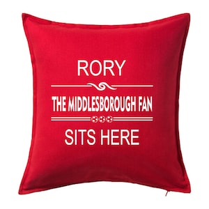 May include: A red square cushion with white text. The text reads "RORY THE MIDDLESBROUGH FAN SITS HERE" with a football graphic. A fan item, likely for a Middlesbrough supporter.