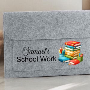 May include: Grey felt folder with a pocket and a colourful illustration of a stack of books and pencils. The text "Samuel's School Work" is printed on the front.