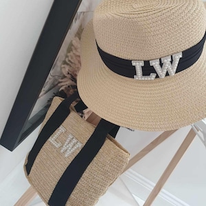 May include: A straw tote bag and a straw hat with black ribbon trim. Both have the initials "LW" in rhinestones.
