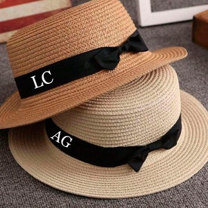 May include: Two straw hats with black ribbon and bows. The top hat has the initials "LC" on the ribbon. The bottom hat has the initials "AG" on the ribbon.