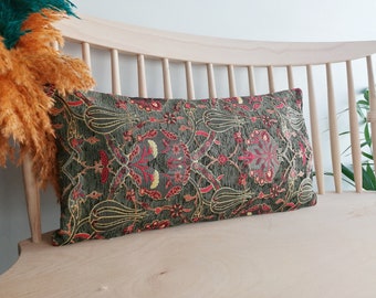 Puede incluir: Un cojín de tiro verde, rojo y dorado con un diseño floral. El cojín está en un banco de madera claro.